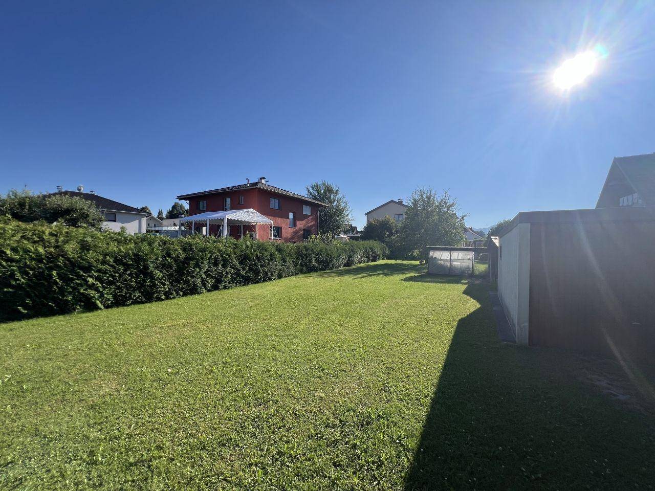 Weitläufige Rasenfläche im Garten mit Heckenbegrenzung und sonnigem Ausblick auf die umliegenden Häuser.
