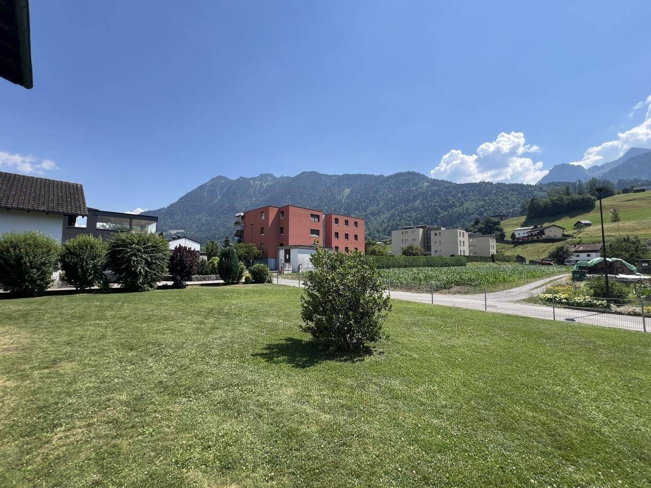 Weitläufiger Gartenbereich mit Blick auf die umliegenden Berge und benachbarte Gebäude.