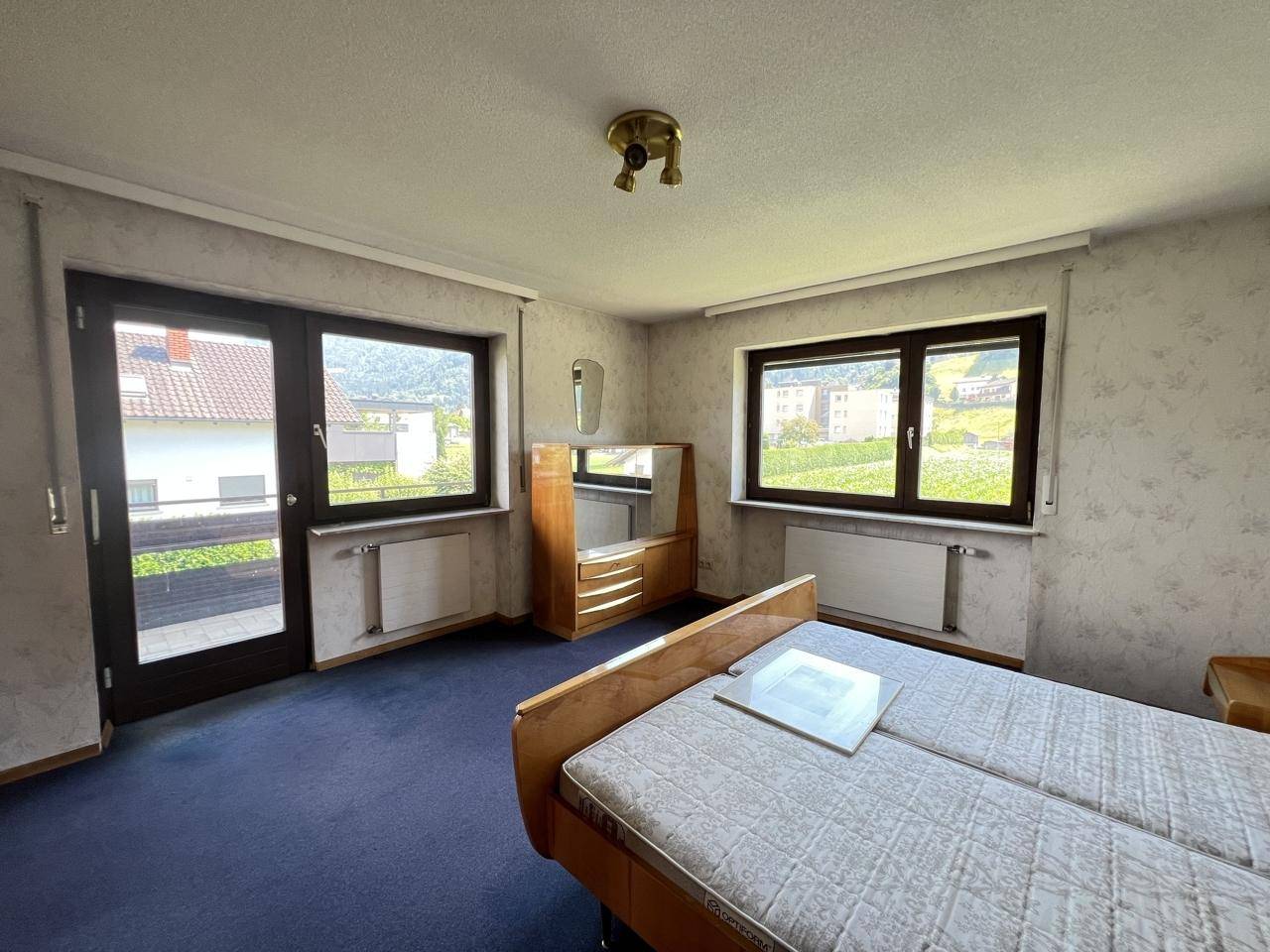 Schlafzimmer mit Teppichboden, Doppelbett und Zugang zu einem kleinen Balkon.