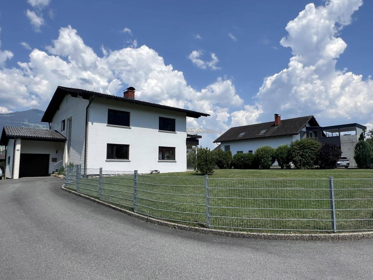 Ansicht des Hauses mit Zufahrt zur Garage und umzäuntem Vorgartenbereich.