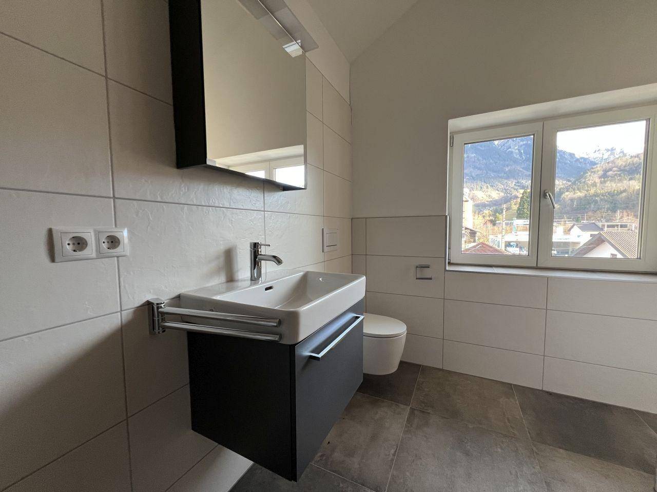 Modernes Badezimmer mit großformatigen Fliesen, Waschtisch und Fenster mit Bergblick.