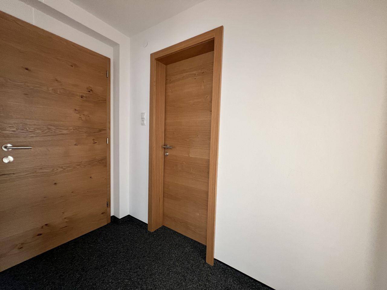 Heller Flur mit Holztüren und dunklem Teppichboden, der zu den Zimmern führt.