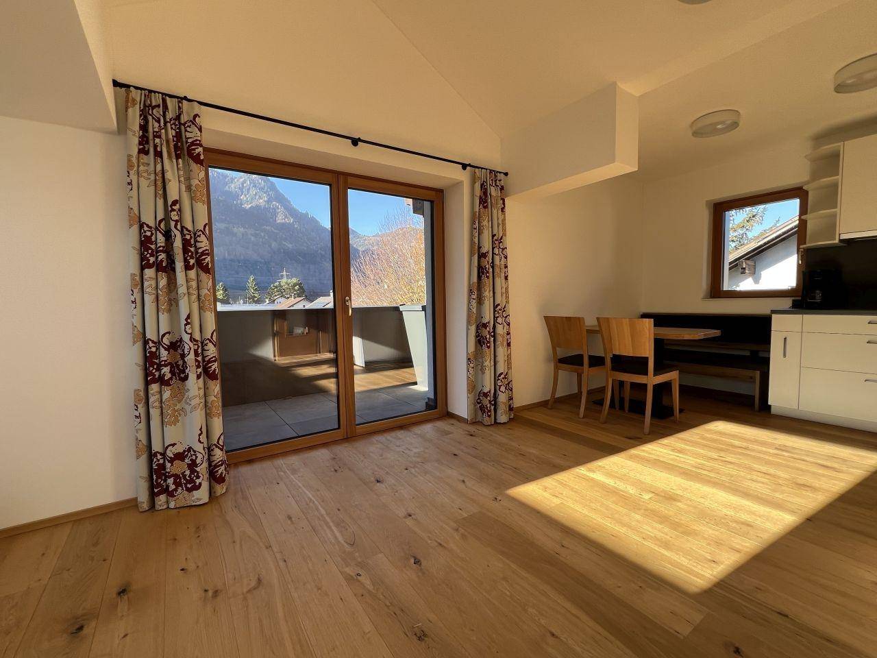 Lichtdurchfluteter Wohn-Essbereich mit Holzboden, Esstisch und großem Balkonzugang mit Bergblick.