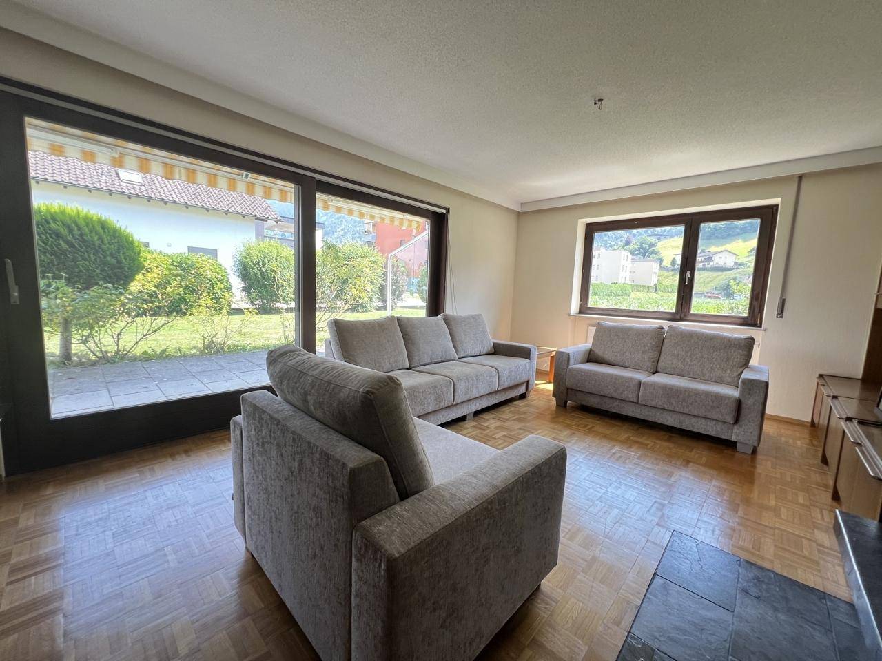 Geräumiges Wohnzimmer mit Parkettboden, großen Fenstern und Zugang zur Terrasse.