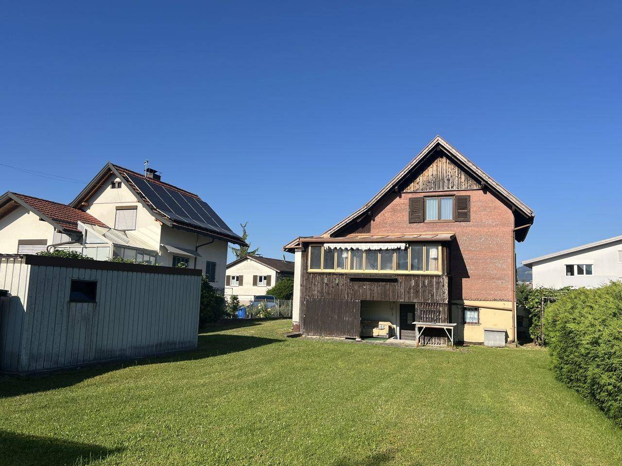 Gepflegter Garten mit Rasenfläche und einem Schuppen, im Hintergrund ein Haus mit Photovoltaikanlage.