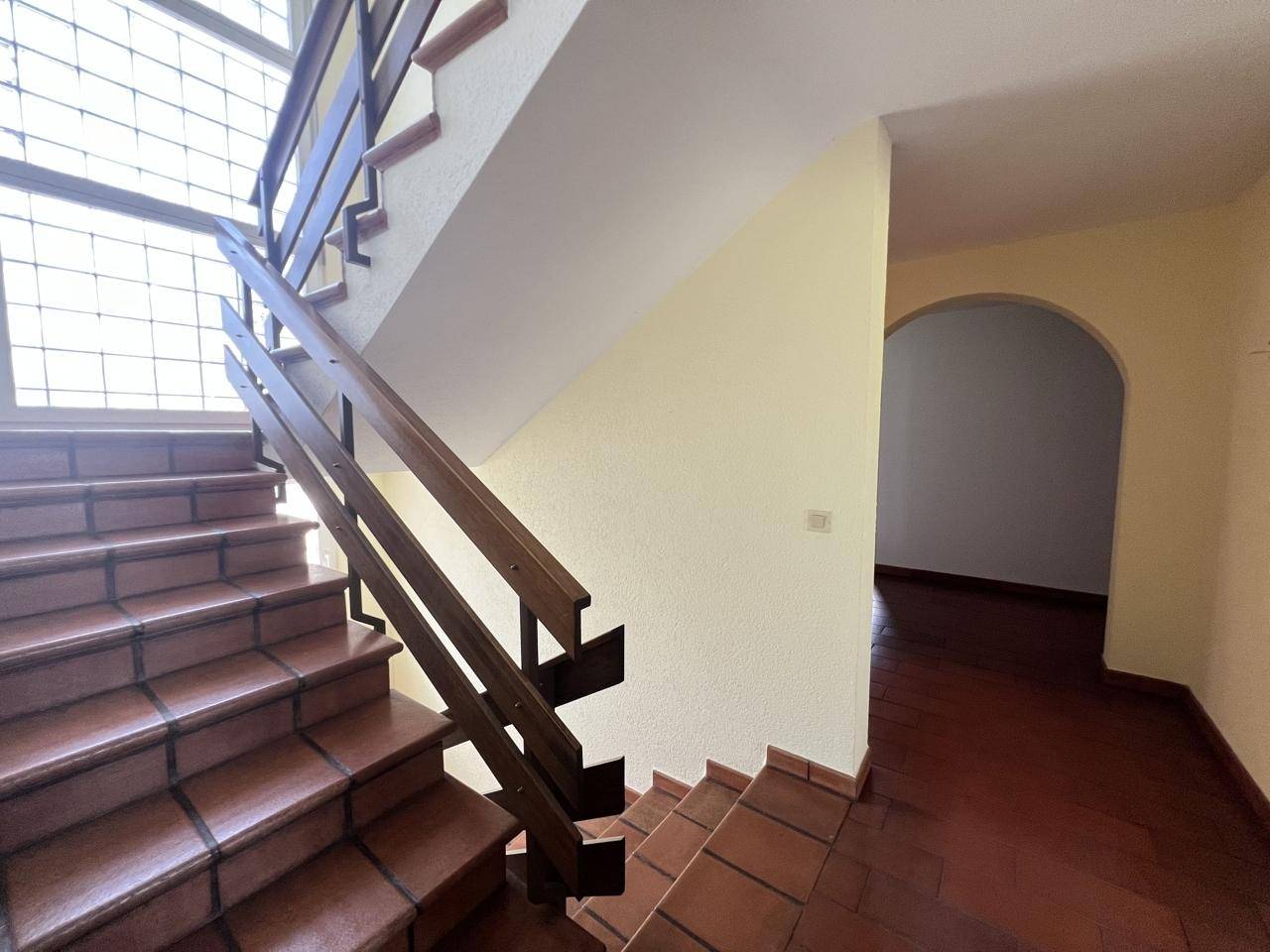 Heller Treppenaufgang mit Holzgeländer und Fliesenboden, führt zu einem angrenzenden Raum.