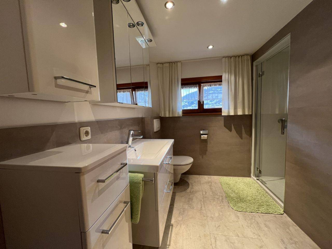 Helles Badezimmer mit Dusche, Waschtisch und Spiegelschrank, in modernen Brauntönen.
