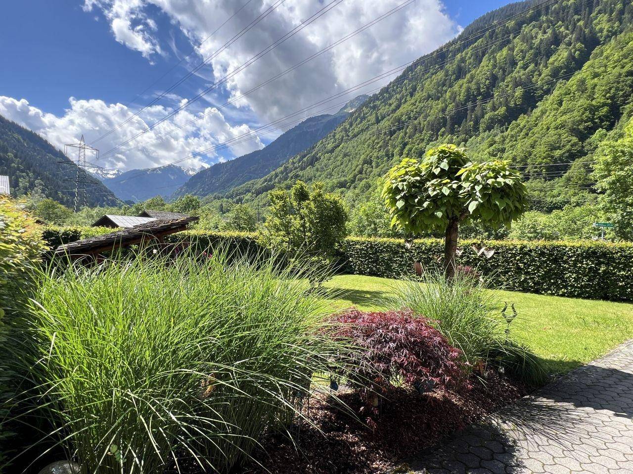 Üppige Gartenbepflanzung mit Blick auf die weite Berglandschaft und den blauen Himmel.