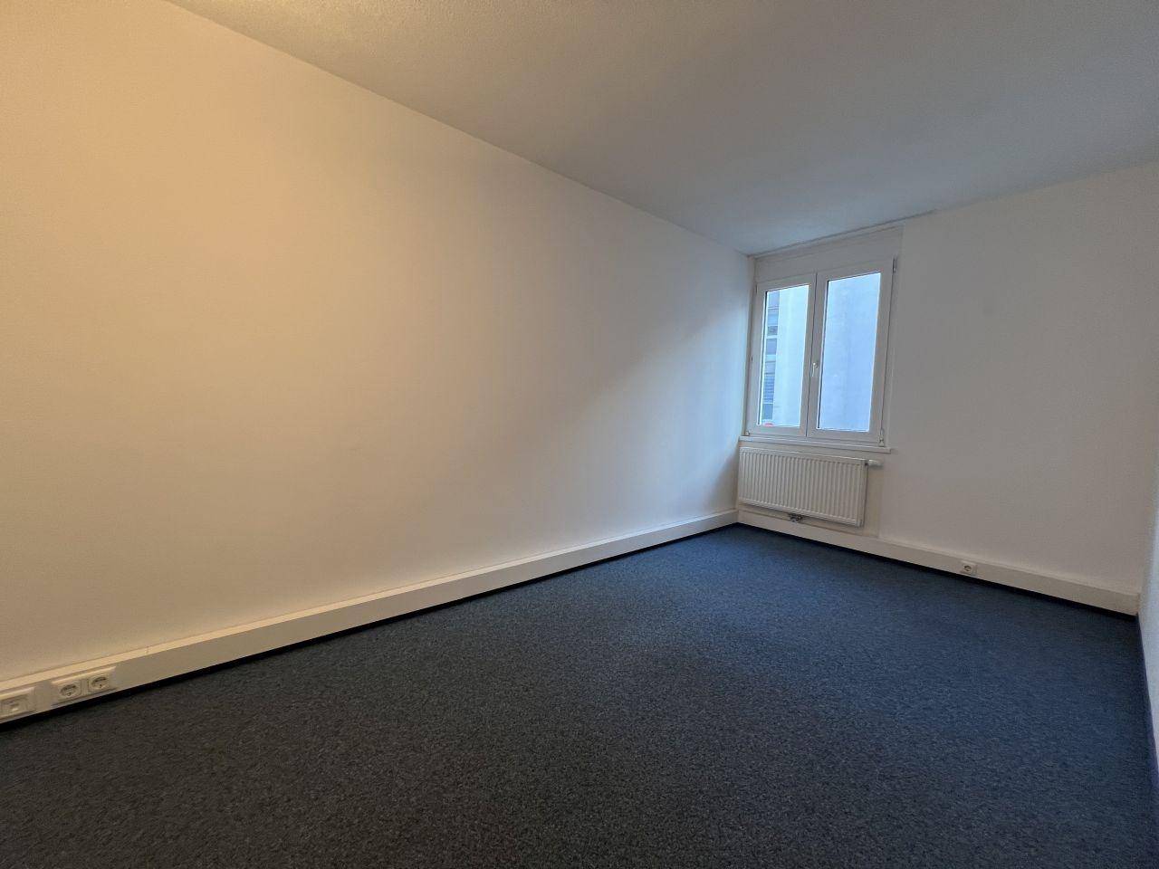 Ruhiges Zimmer mit blauem Teppichboden und einem Fenster, geeignet als Arbeits- oder Schlafzimmer.