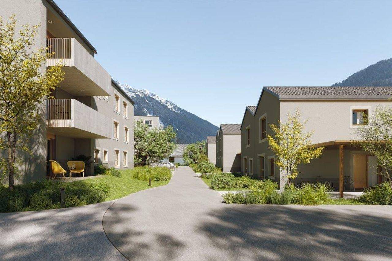 Wohnanlage mit modernen Gebäuden und Zufahrtsstraße, umgeben von Bergen und Natur.