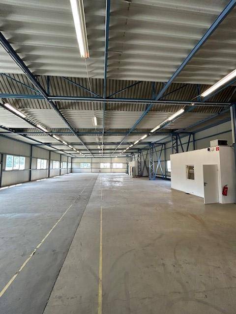 Weitläufige Lagerhalle mit Betonboden, sichtbaren Deckenstrukturen und einem kleinen abgetrennten Bereich.