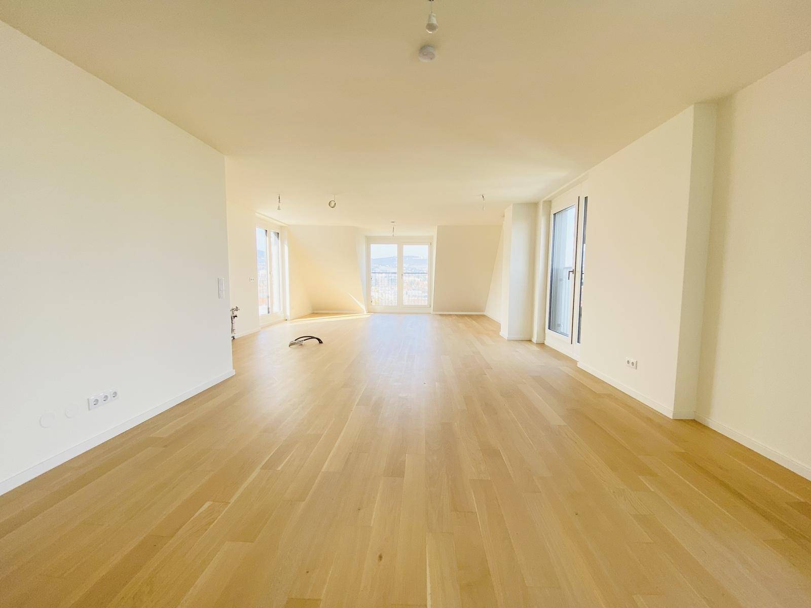 Helles, leeres Zimmer mit Holzboden und großen Fenstern, bereit für die individuelle Gestaltung.