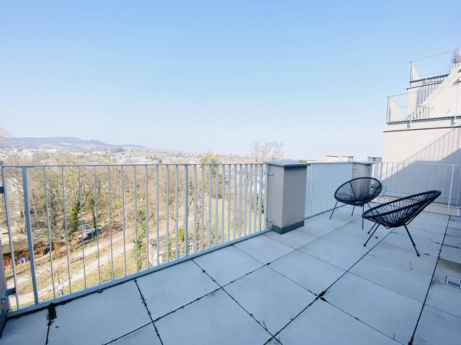 Große Terrasse mit Metallgeländer und Panoramablick über die Stadt und bewaldete Hügel.