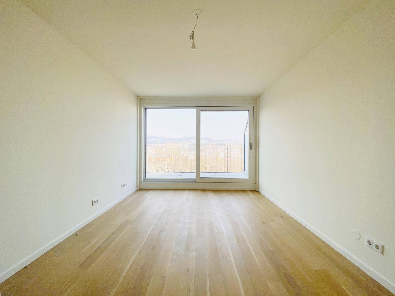 Lichtdurchfluteter Raum mit weitem Ausblick durch große Fenster und hellem Holzparkettboden.