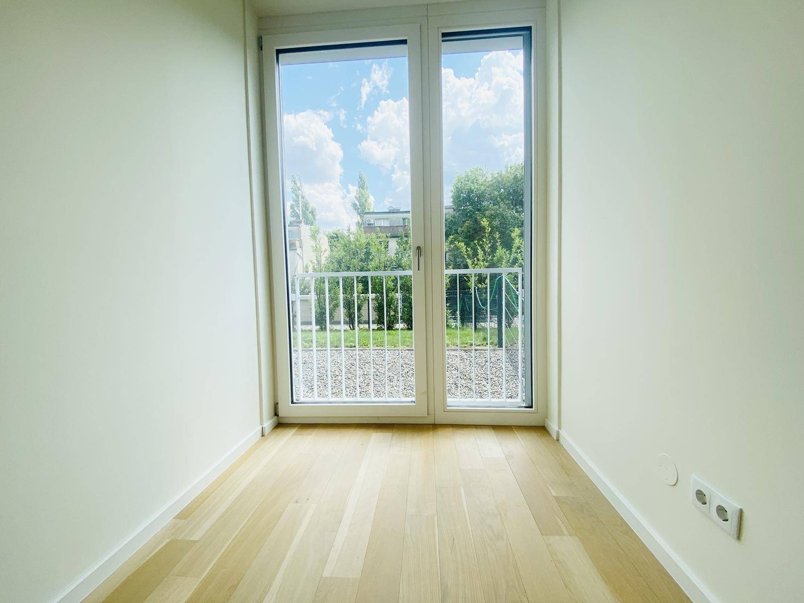 Kleineres Zimmer mit hellem Parkettboden und großen Fenstern mit Blick ins Grüne.