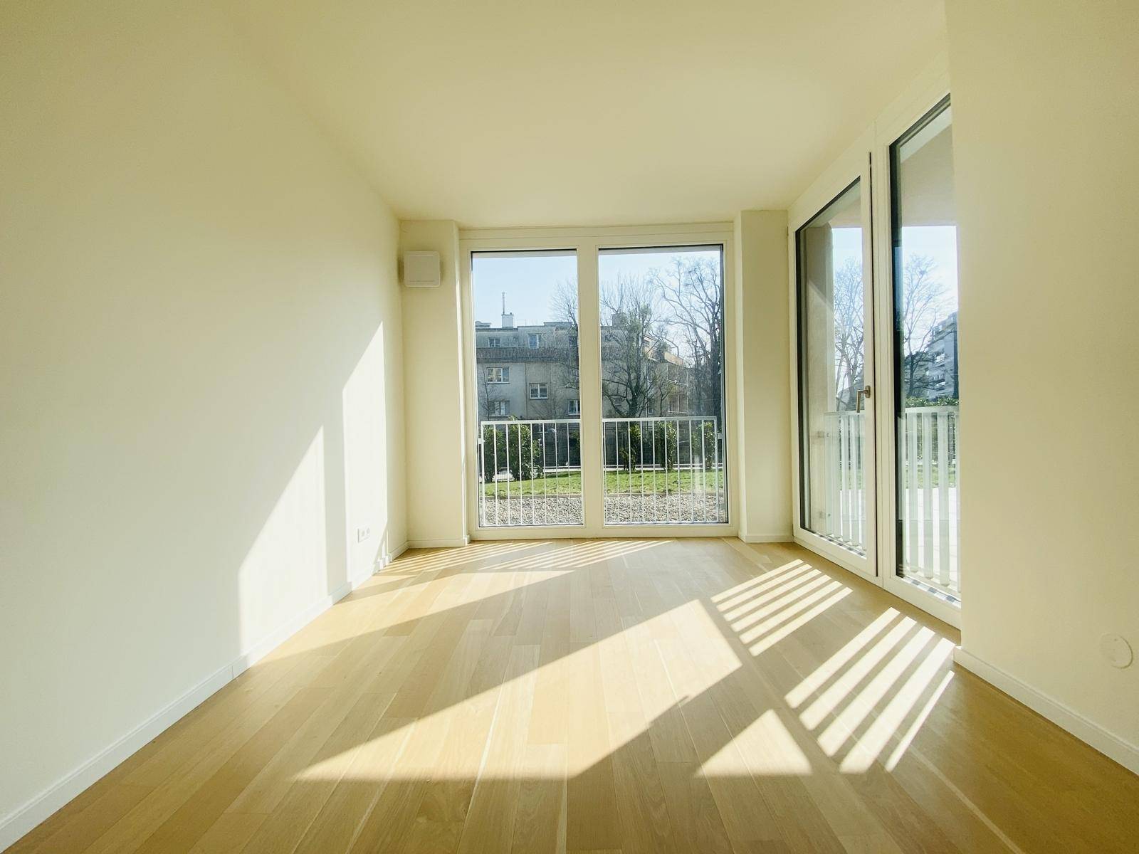 Helles Zimmer mit Parkettboden, großen Fenstern und Zugang zu einem französischen Balkon.