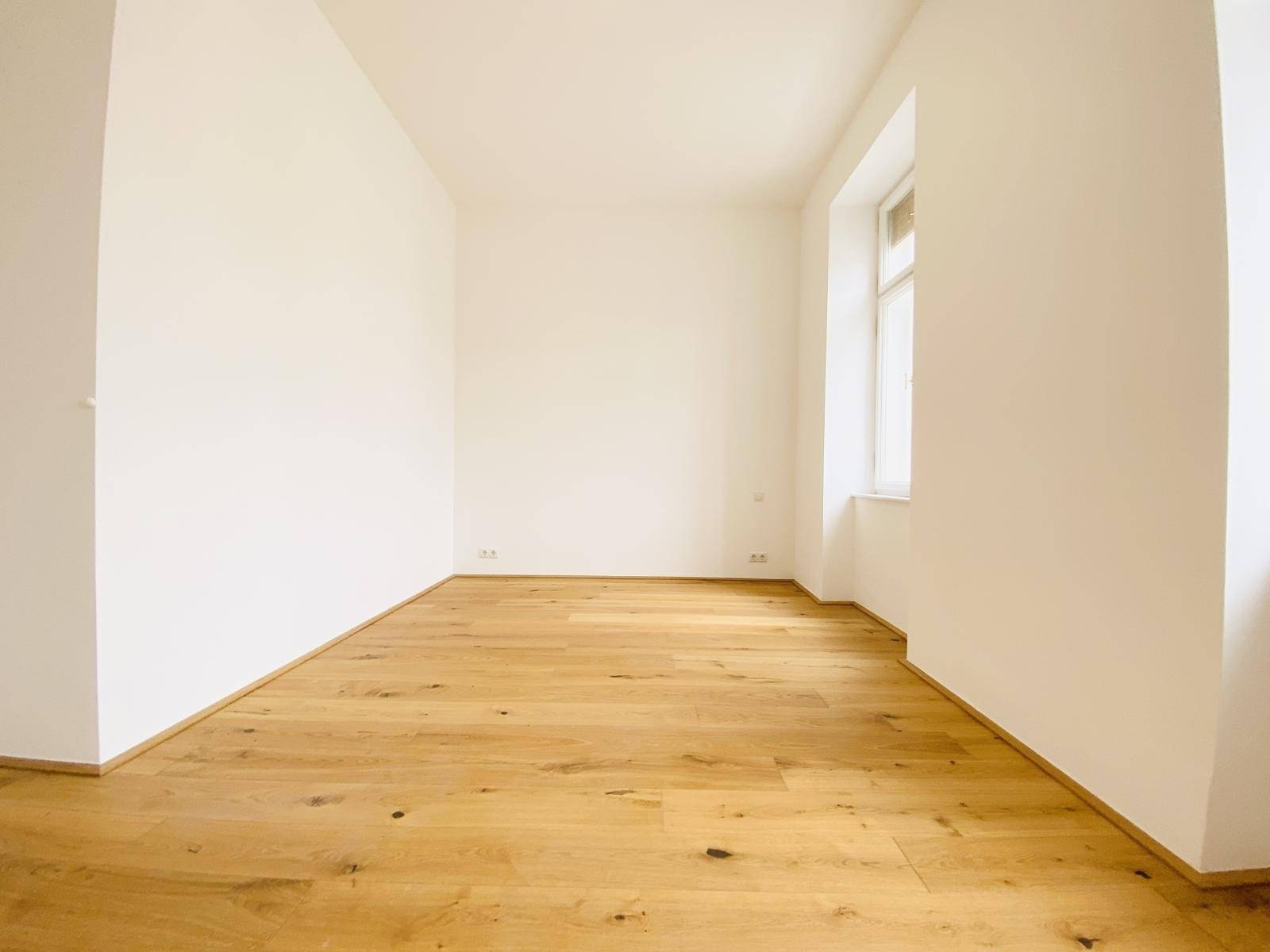 Helles Zimmer mit Holzboden und einem Fenster, ideal als Schlaf- oder Arbeitszimmer.
