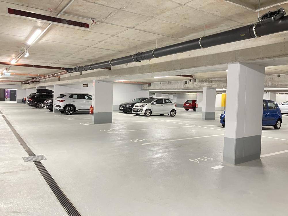 Helle Tiefgarage mit vielen Parkplätzen und sichtbaren Deckeninstallationen.