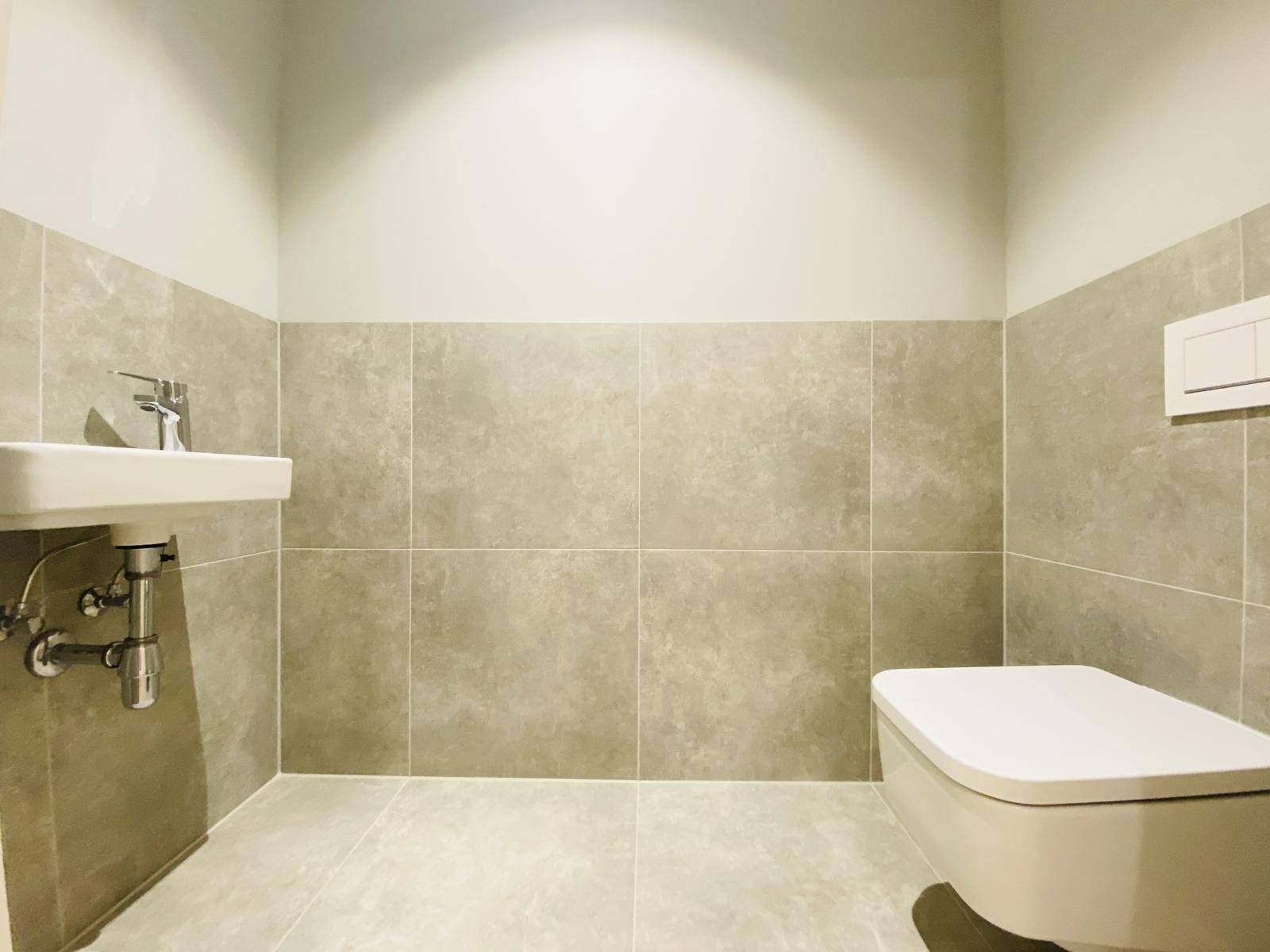 Modernes Gäste-WC mit Wand-WC und kleinem Waschbecken, halbhoch gefliest.