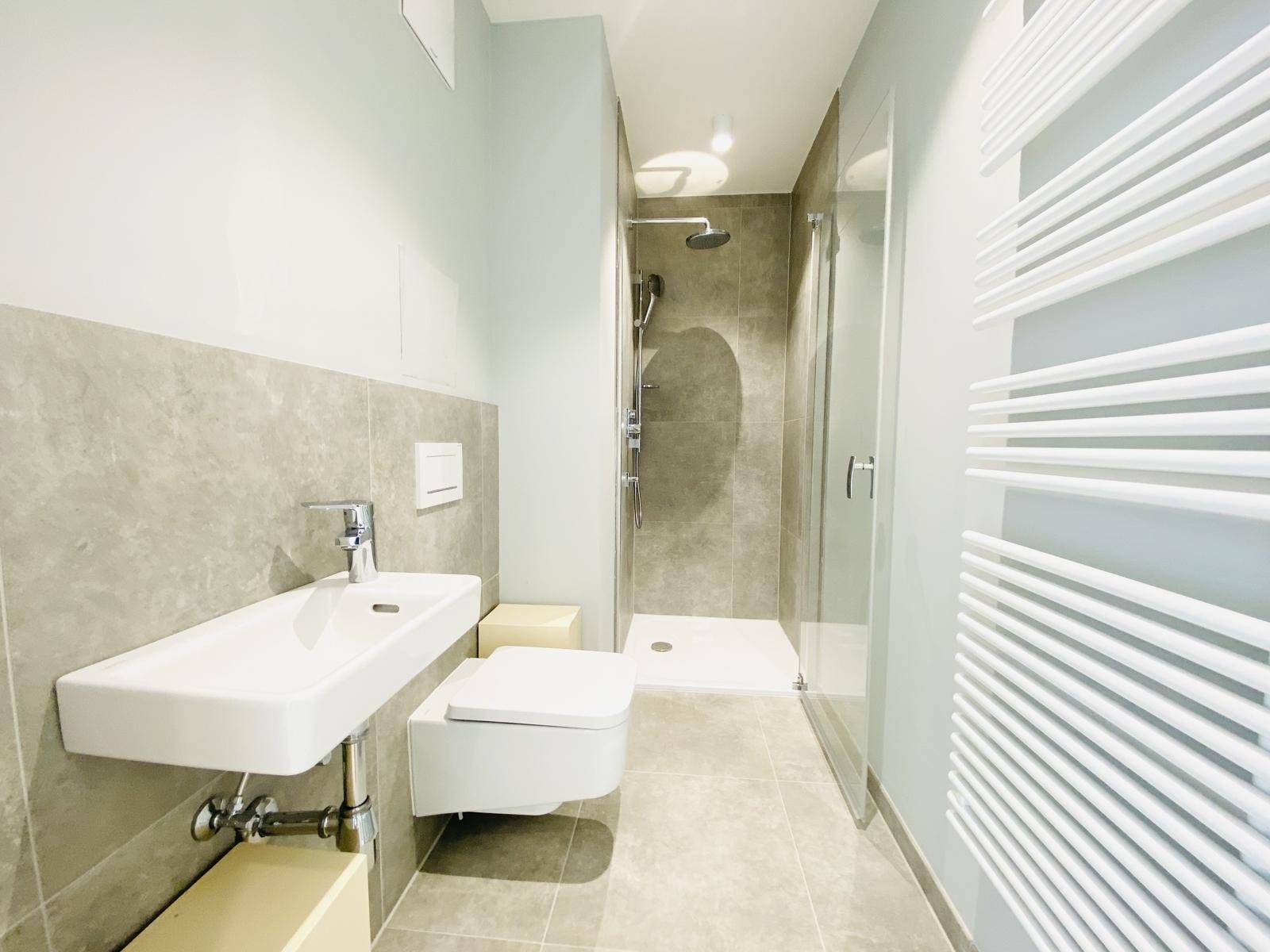 Modernes Badezimmer mit Dusche, Wand-WC und beheiztem Handtuchhalter in neutralen Farbtönen.