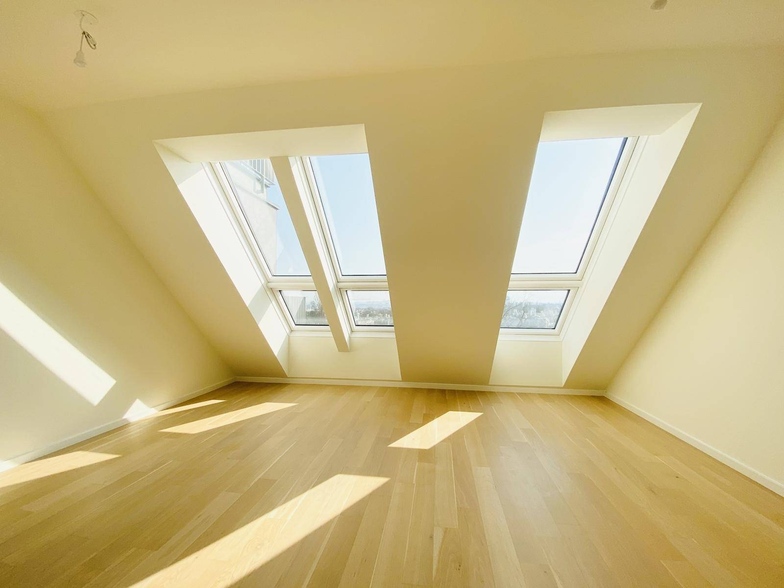 Helles Dachgeschosszimmer mit schrägen Wänden, Holzparkettboden und mehreren Dachfenstern.
