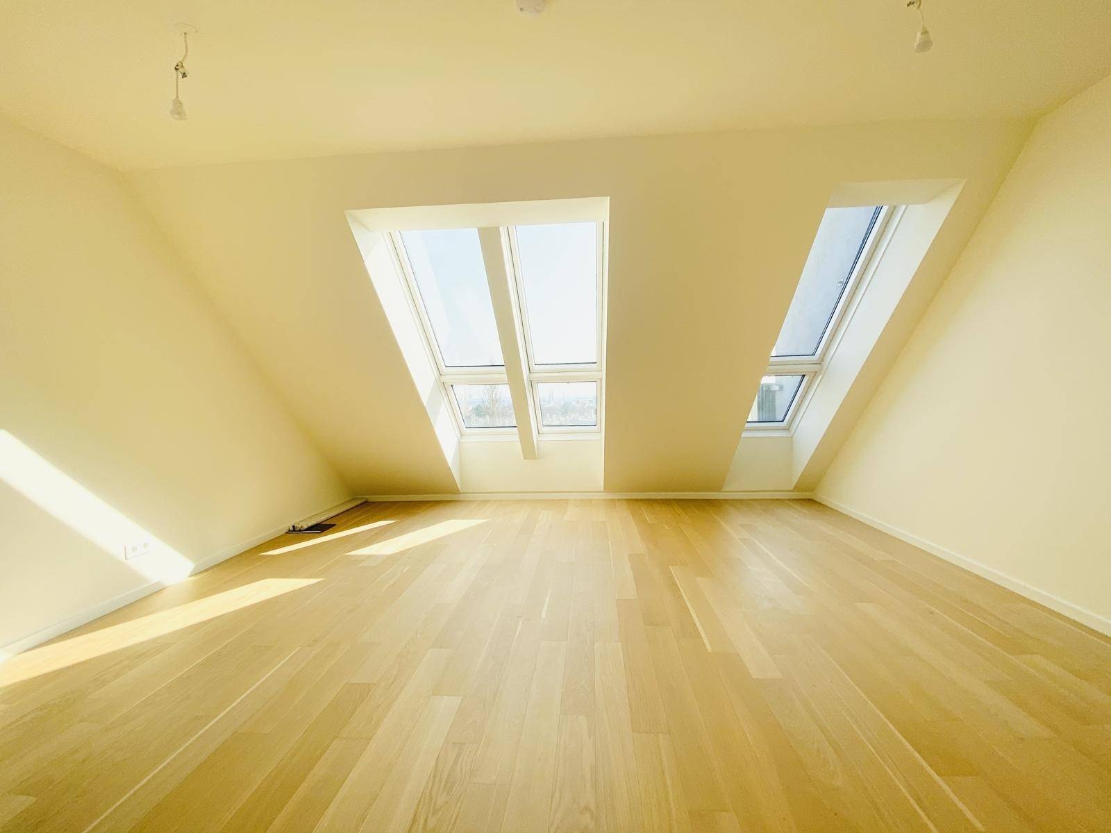 Helles Dachgeschosszimmer mit schrägen Wänden, Holzparkettboden und mehreren Dachfenstern.