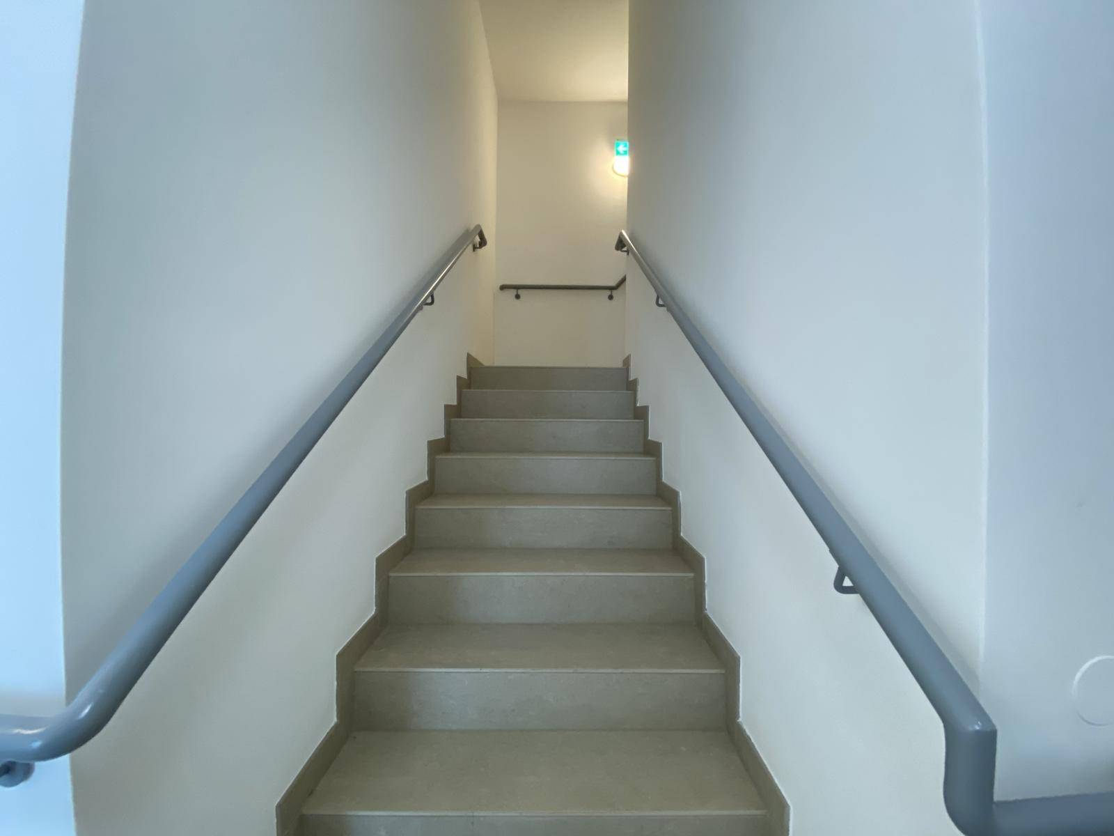 Treppenhaus mit Handläufen und gefliesten Stufen, führt zu den oberen Etagen.