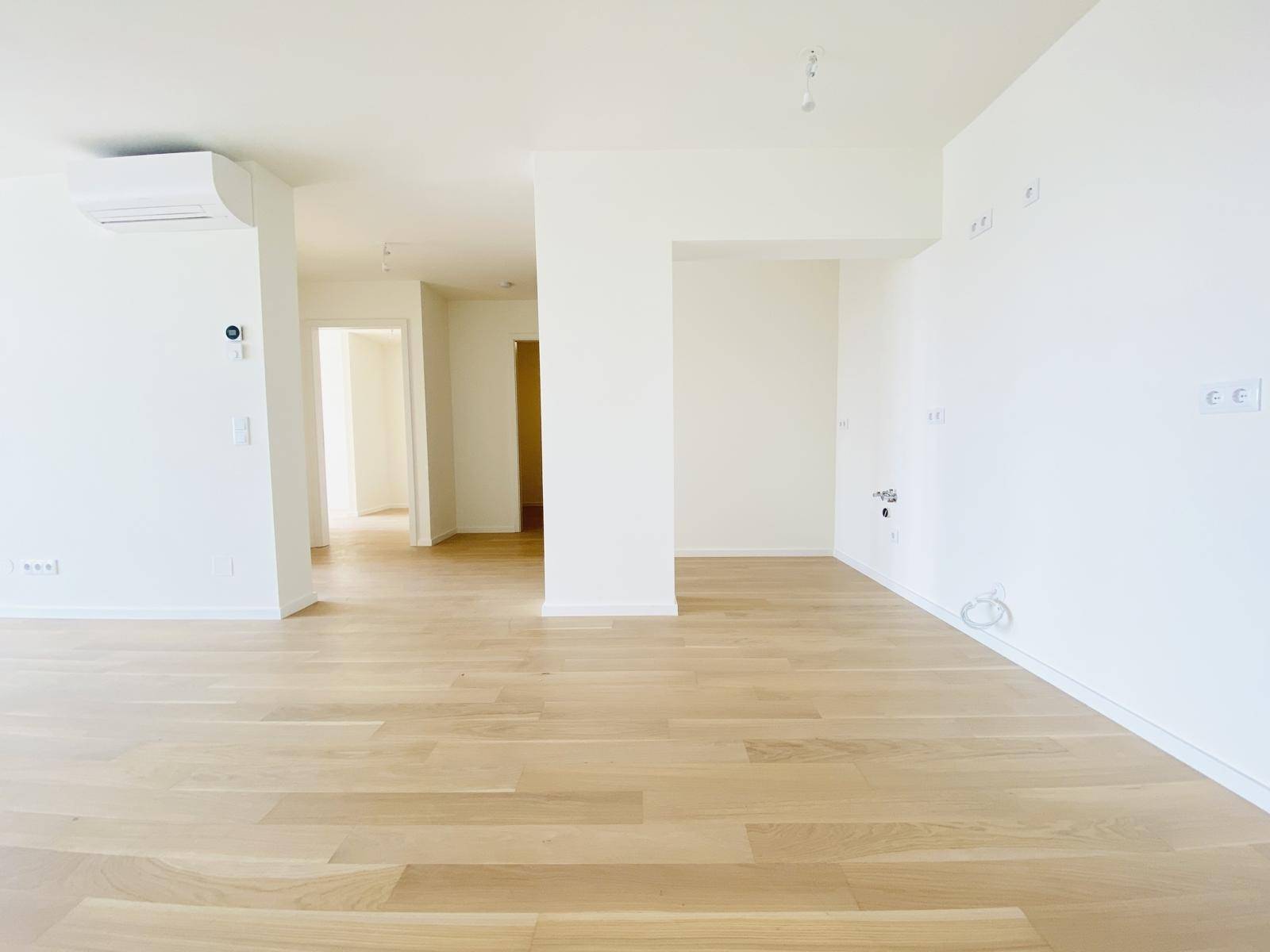 Geräumiger, heller Wohnbereich mit Holzboden und Vorbereitung für Klimaanlage.