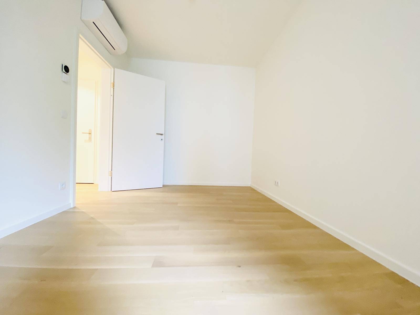 Helles Schlafzimmer mit Parkettboden und Klimaanlage, bereit zum Einrichten.