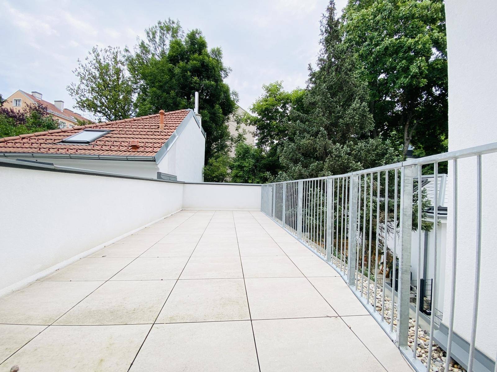 Weitläufige Terrasse mit hellem Fliesenboden, Metallgeländer und Blick ins Grüne.