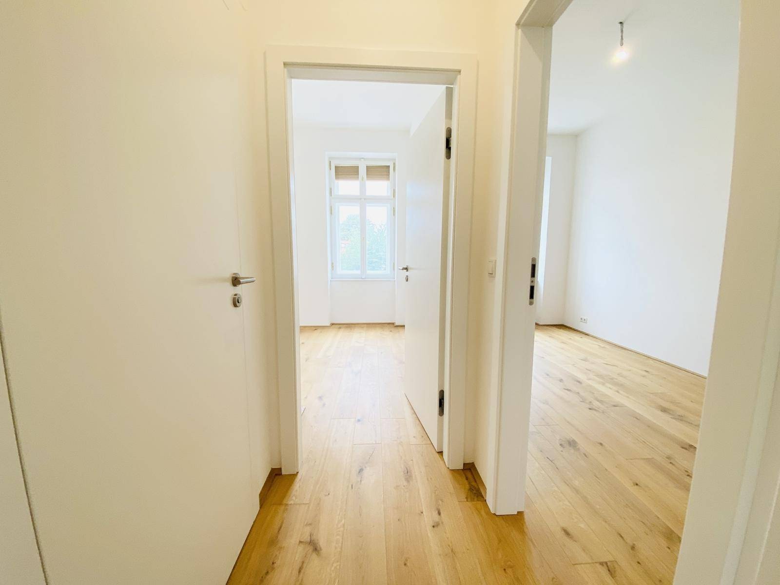 Flur mit Holzboden, der zu verschiedenen Zimmern führt, darunter ein Schlafzimmer.
