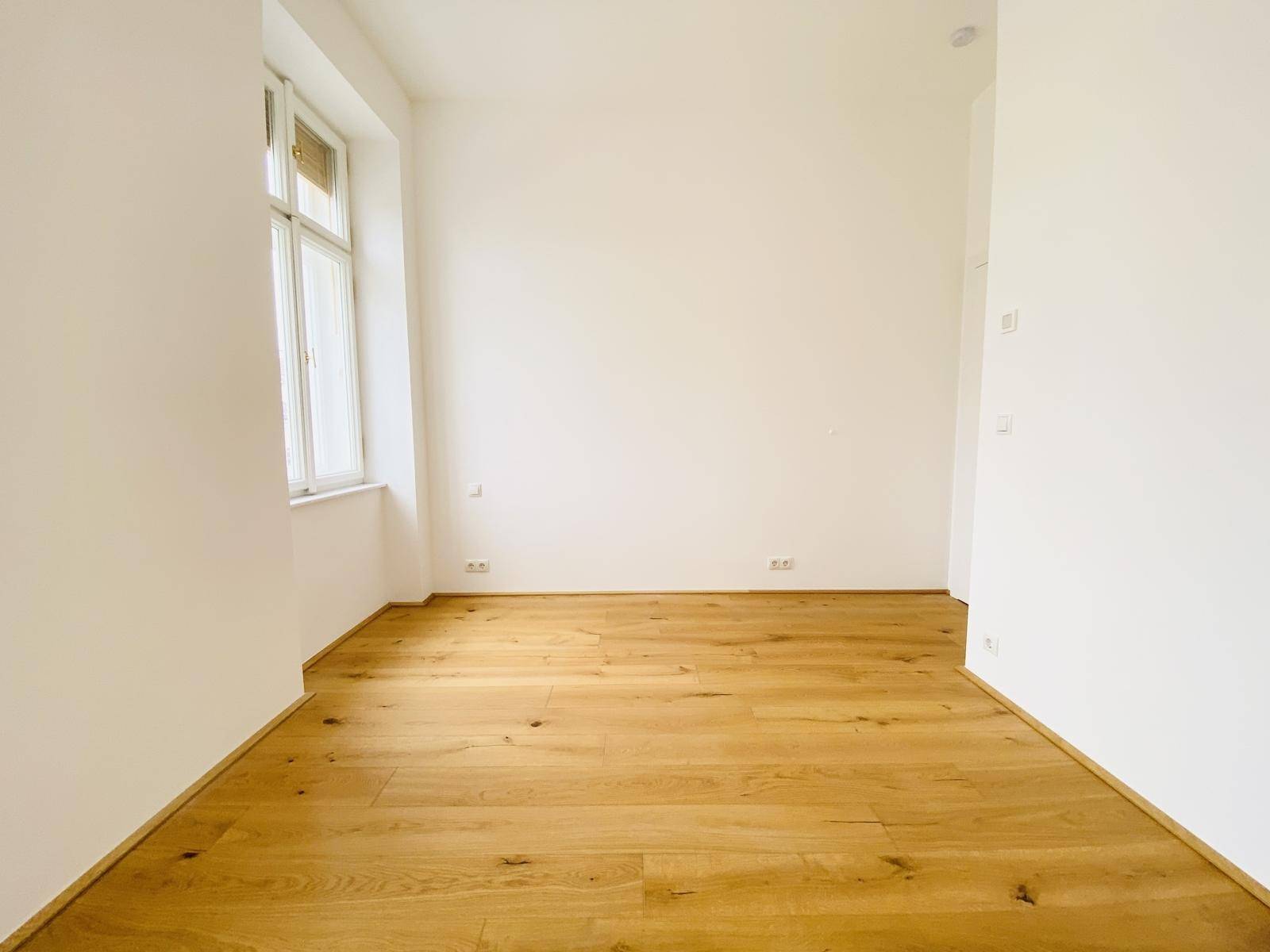 Geräumiges Schlafzimmer mit Holzboden und einem großen Fenster, das viel Licht bietet.