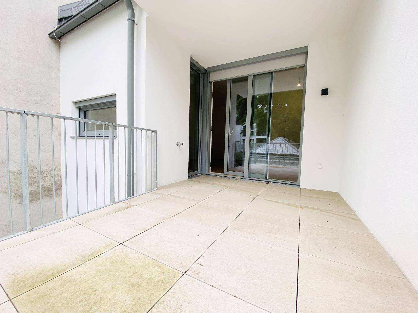 Großer Balkon mit Fliesen und Schiebetüren, die zum Innenraum führen.