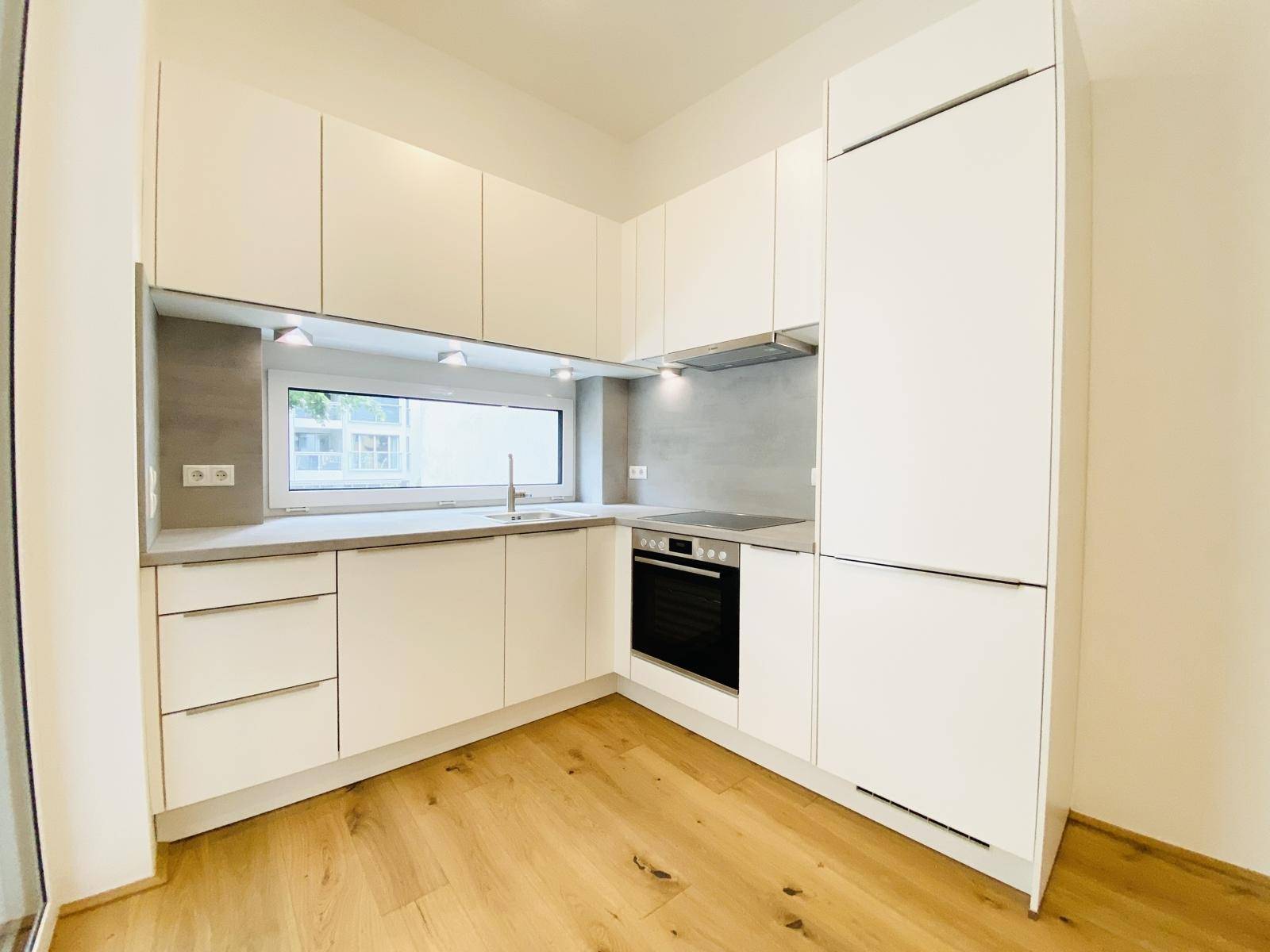 Moderne Einbauküche mit weißen Schränken, integrierten Geräten und einem Fenster.