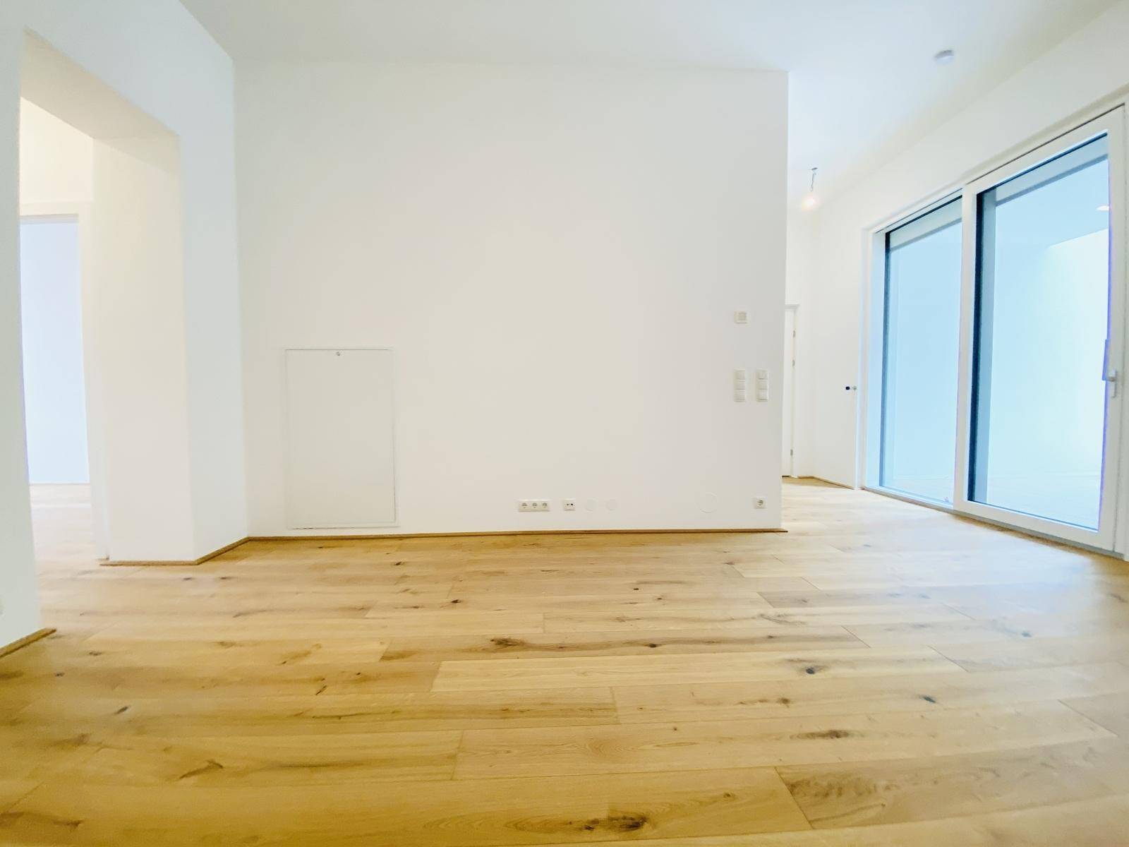 Geräumiges, helles Wohnzimmer mit Holzboden und großen Schiebetüren zum Balkon.