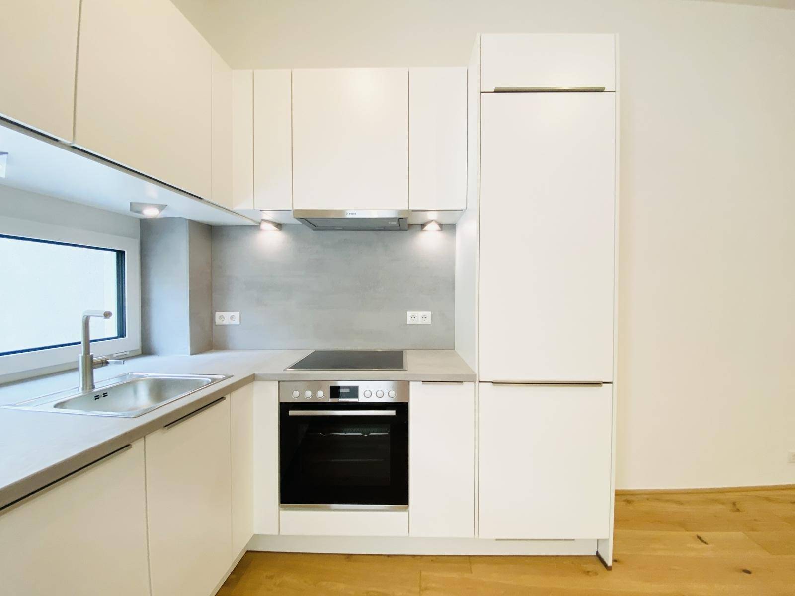 Kompakte, moderne Küche mit weißen Schränken, integriertem Backofen und Kochfeld.
