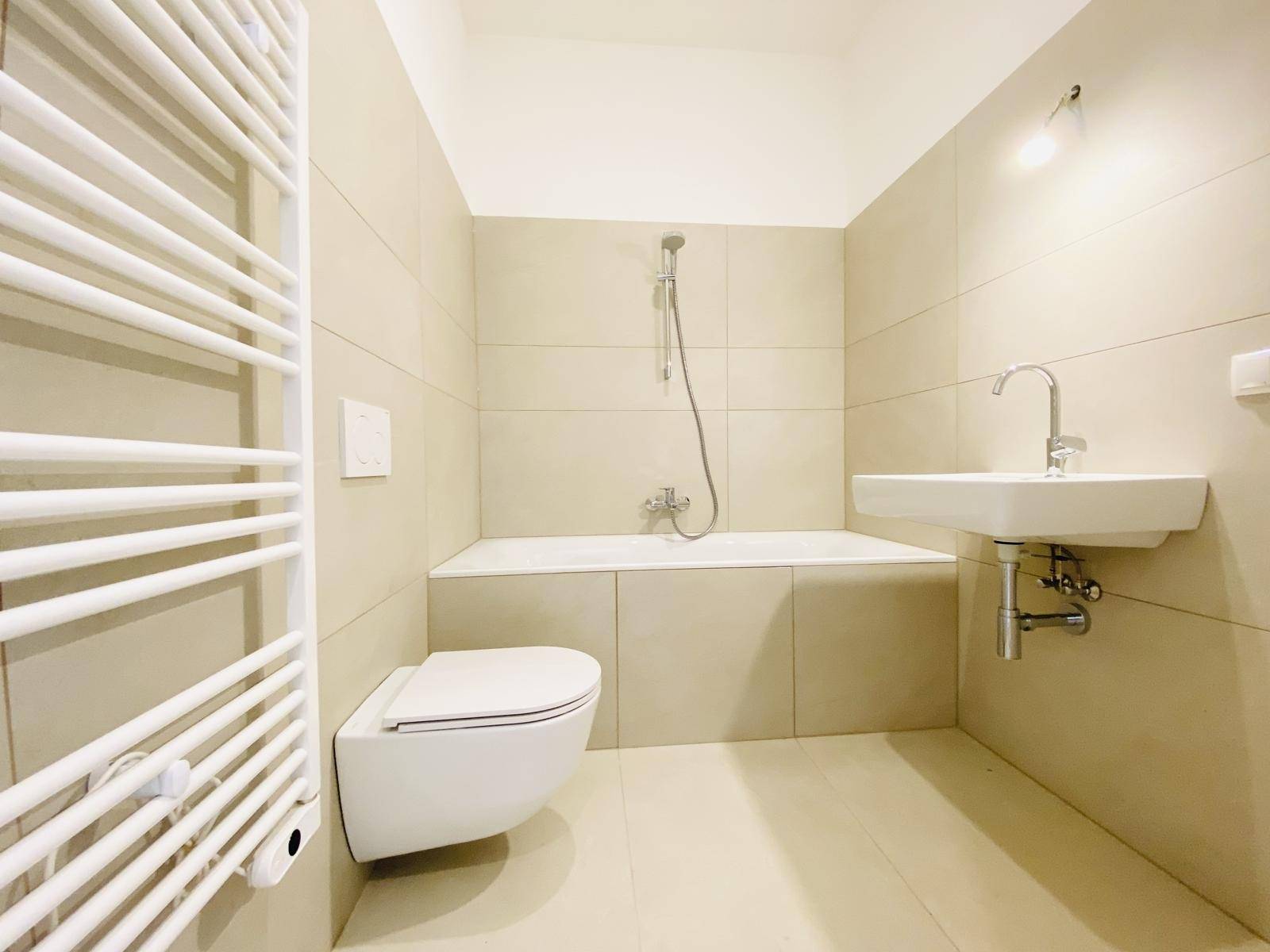 Modernes Badezimmer mit beigefarbenen Fliesen, Badewanne, Toilette und Handtuchheizkörper.