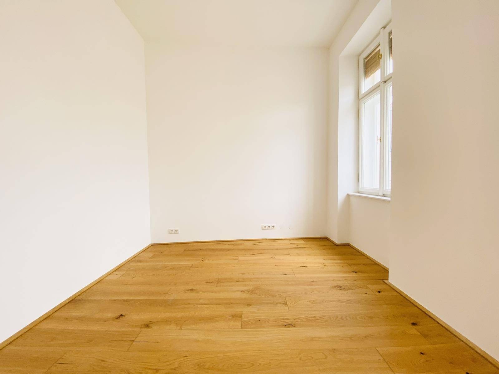 Helles Schlafzimmer mit Holzboden und einem Fenster, das eine ruhige Atmosphäre schafft.