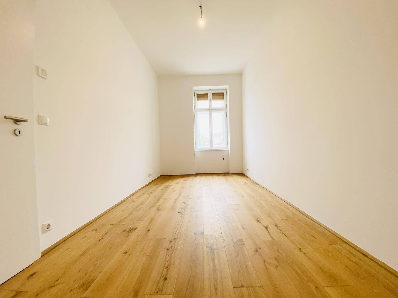 Helles Schlafzimmer mit Holzboden und einem Fenster, das viel Tageslicht hereinlässt.