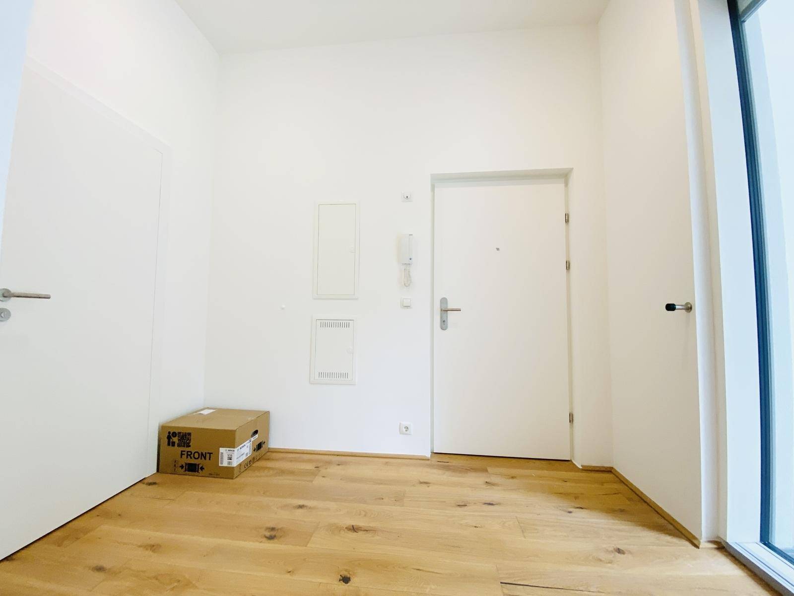 Heller Eingangsbereich einer Wohnung mit Holzboden und weißer Tür.
