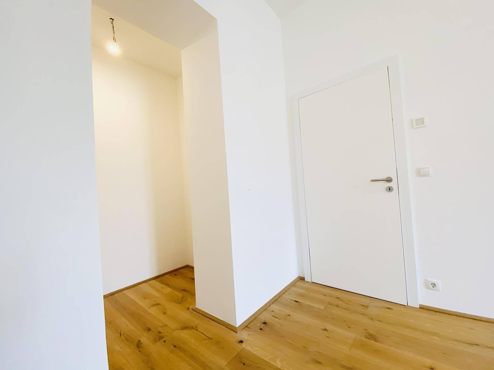 Heller Bereich mit Holzboden und weiß gestrichenen Wänden, der zu einem weiteren Raum führt.