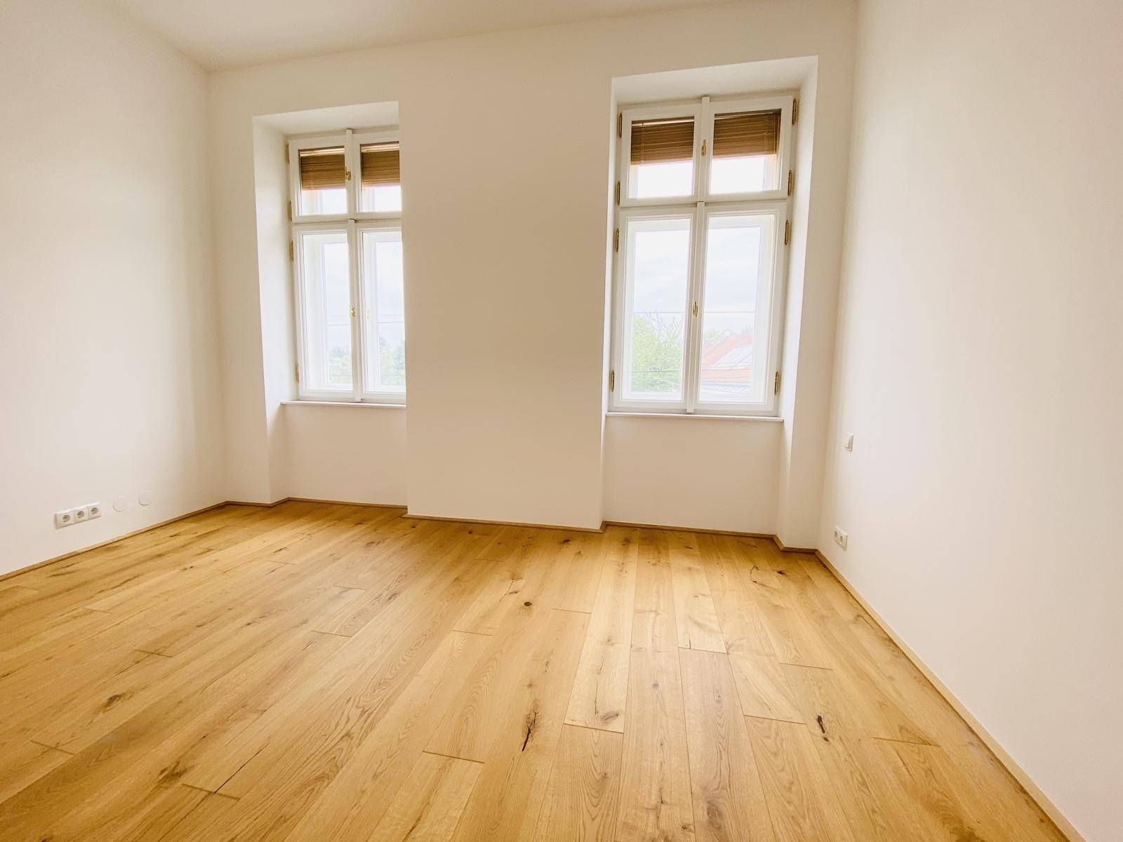 Helles Schlafzimmer mit Holzboden und zwei Fenstern, die eine angenehme Belichtung bieten.