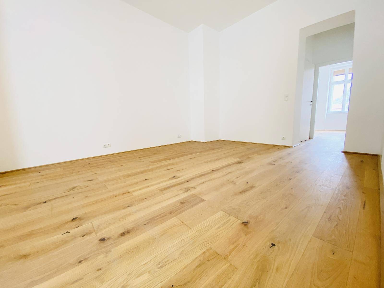 Leeres Wohnzimmer mit warmem Holzboden und weißen Wänden, bereit zur Gestaltung.