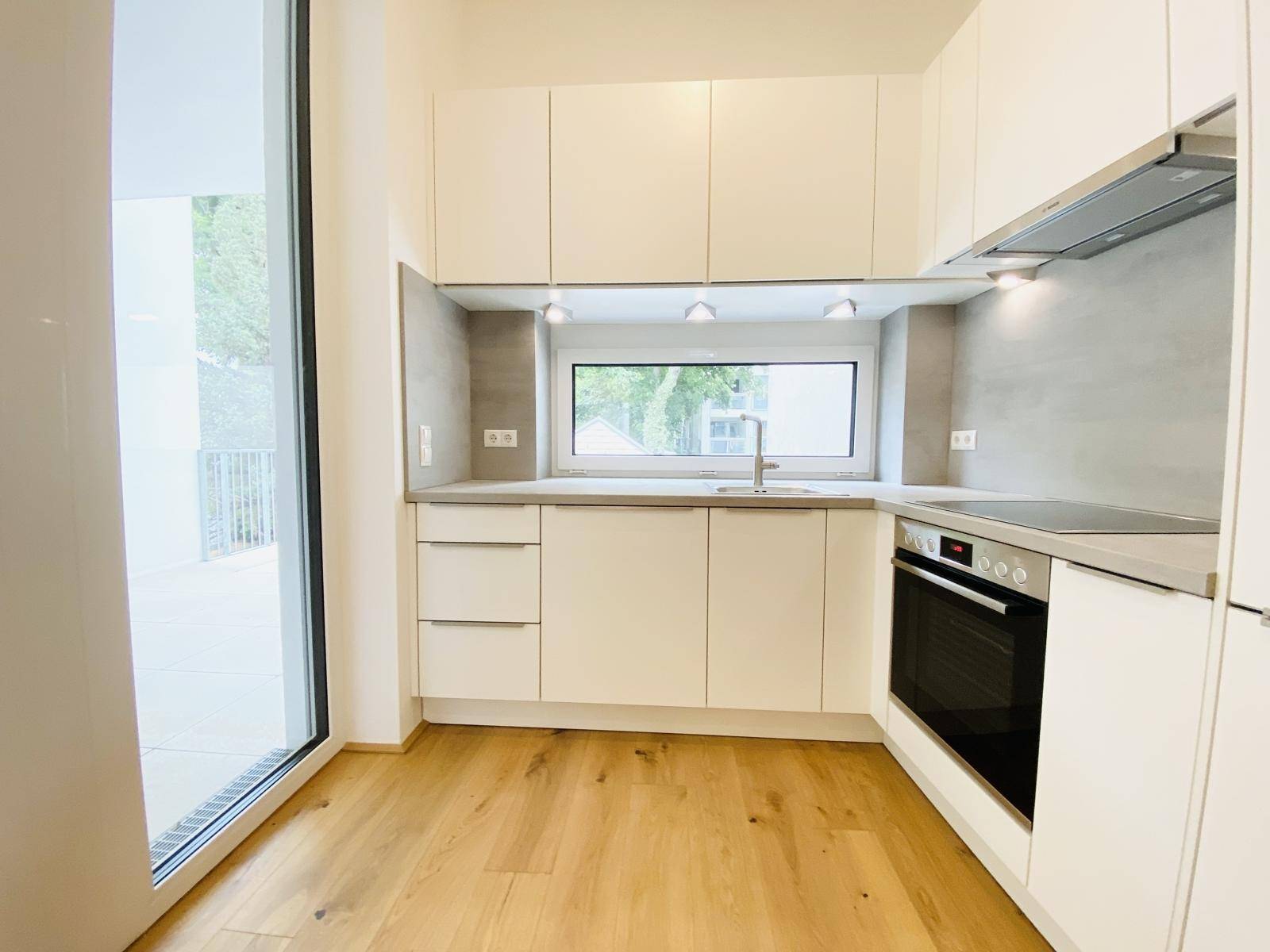 Helle, moderne Küche mit weißen Fronten, Spüle unter dem Fenster und Balkonzugang.