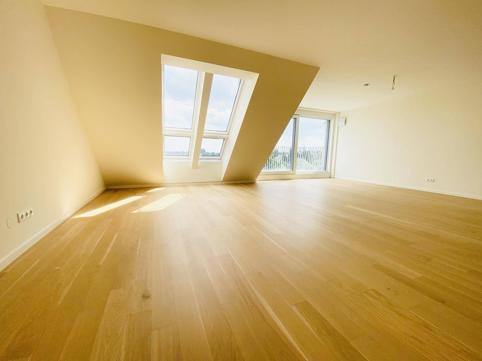Heller Wohnraum mit Dachschrägen, großen Fenstern und Holzboden, bietet viel natürliches Licht und Ausblick.