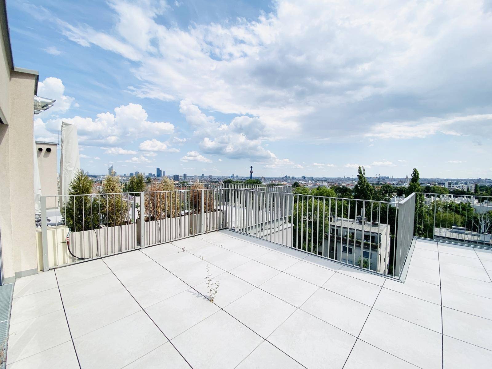 Dachterrasse mit Fliesenboden, Pflanzen in Kübeln und Panoramablick über die Stadtlandschaft.