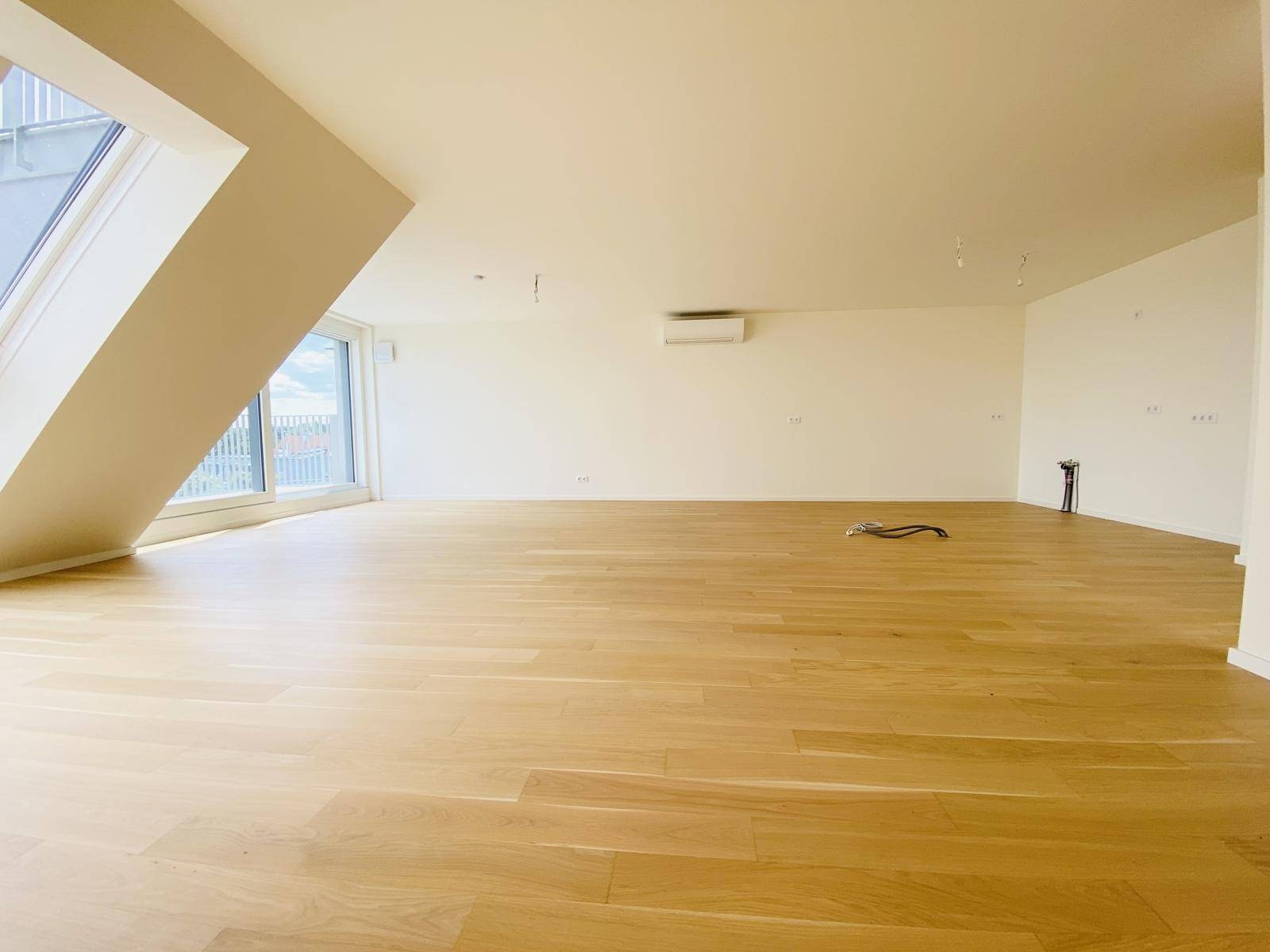 Großer, leerer Wohnraum mit Holzboden und Klimaanlage, bereit für individuelle Gestaltung.