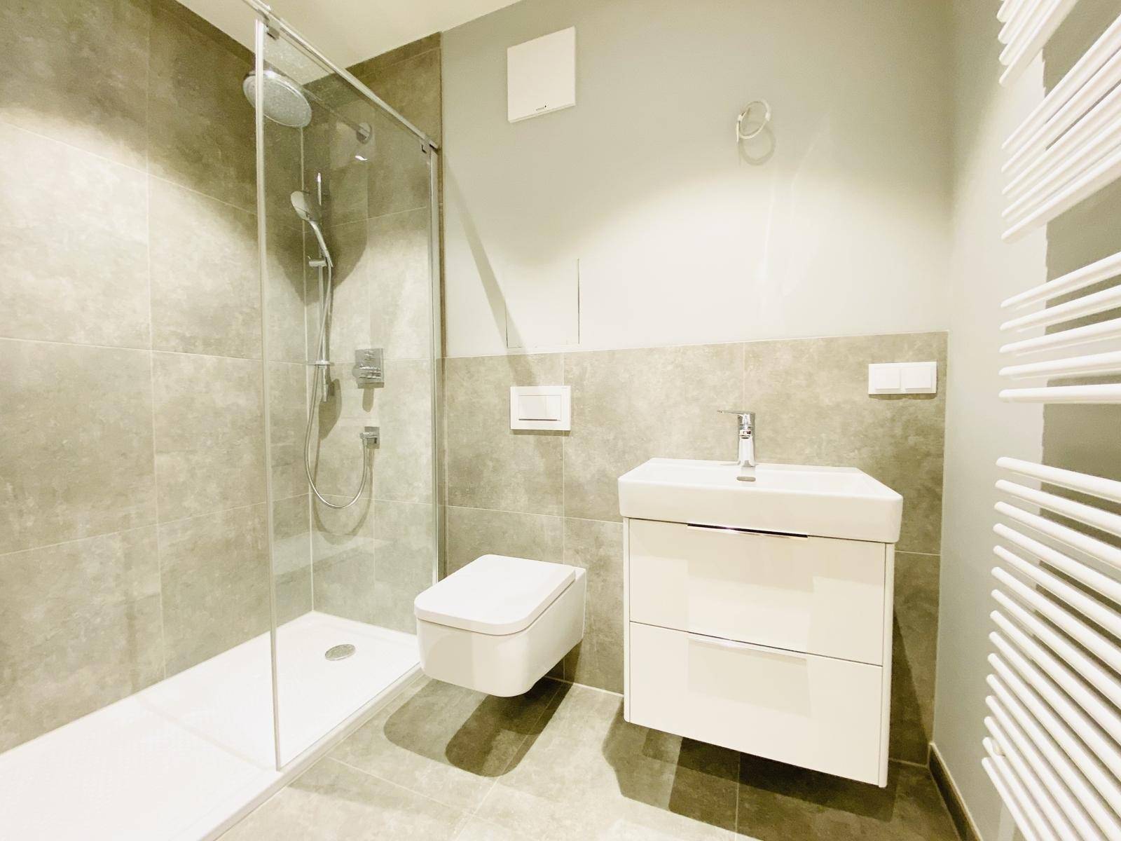 Modernes Badezimmer mit grauen Fliesen, ebenerdiger Dusche und wandhängendem WC.