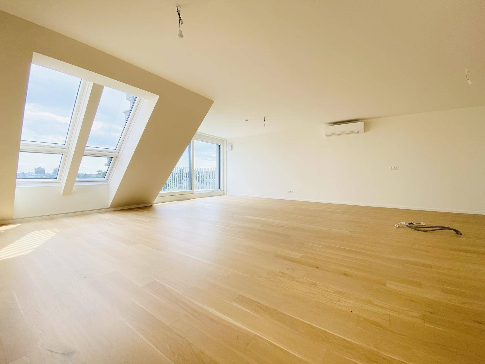 Geräumiger Wohnbereich mit Holzboden, Dachfenstern und Klimaanlage, ideal für modernes Wohnen.