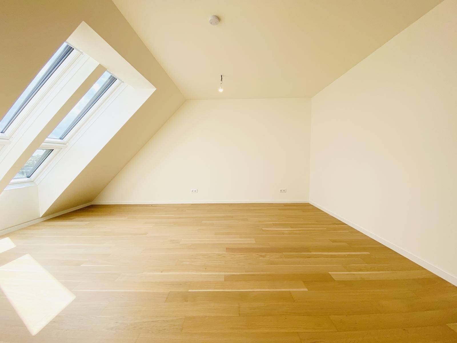 Lichtdurchfluteter Raum im Dachgeschoss mit Holzboden und großem Dachfenster.